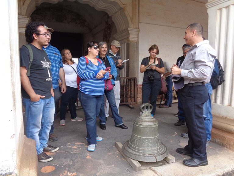 Los participantes escuchan al historiador, se observa la Casa de Alcántara, segunda sede de la Universidad.