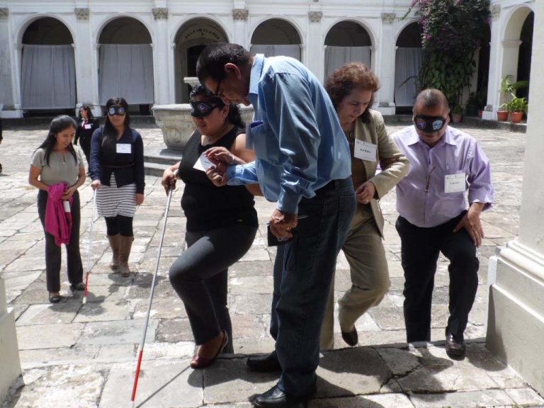 Talleristas intentan caminar con los ojos cubiertos por el claustro del MUSAC, dirigidos por personas con los ojos descubiertos, para experimentar la discapacidad visual.